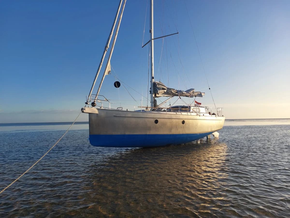 An aluminium Bestevaer 36 rests upright on exposed tidal ground in low evening light.