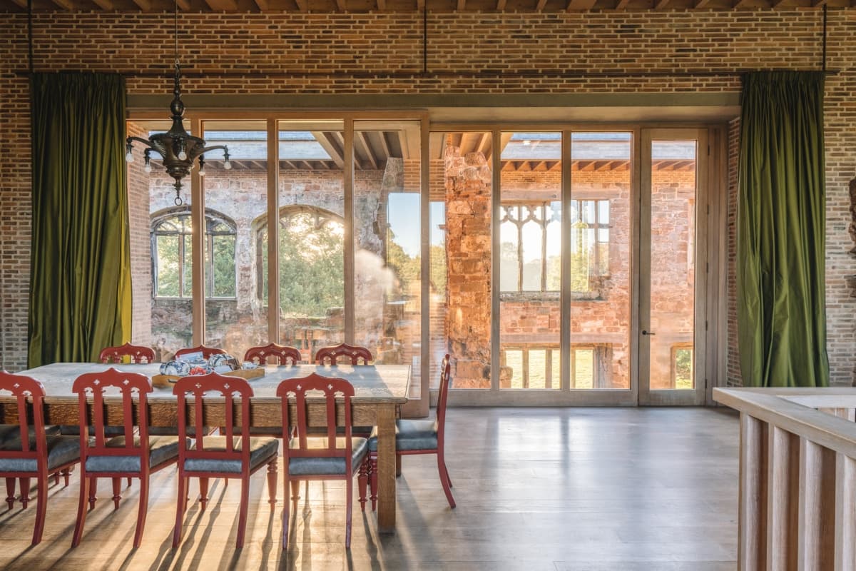 A dining table inside Astley Castle where warm new brick and glass meet weathered ruin walls.