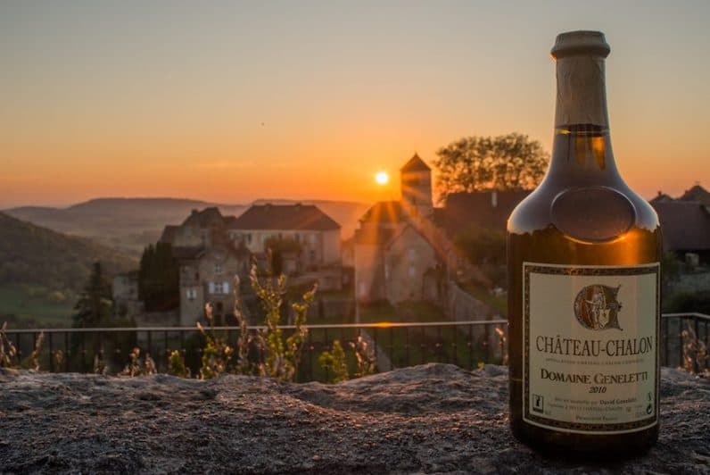 A 2010 Château-Chalon vin jaune in its clavelin bottle at sunset with the hilltop village behind it.