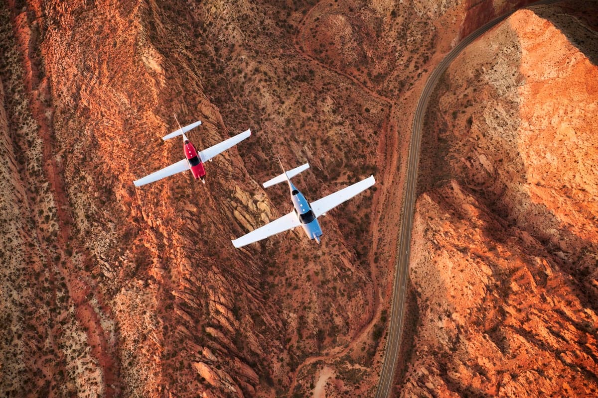 Two Cirrus SR aircraft photographed in flight above a reddish canyon landscape.