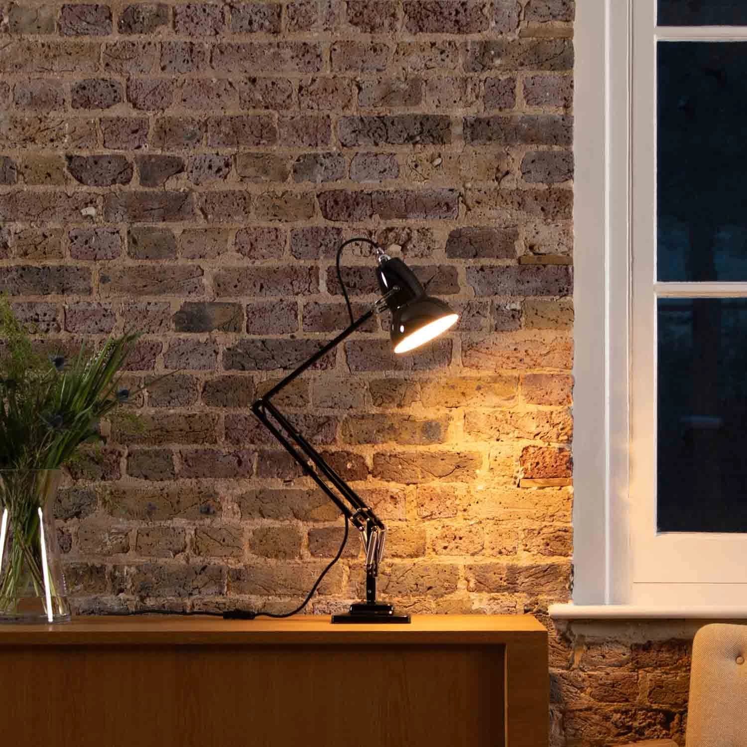 A black Anglepoise Original 1227 illuminates a brick wall above a wooden sideboard.