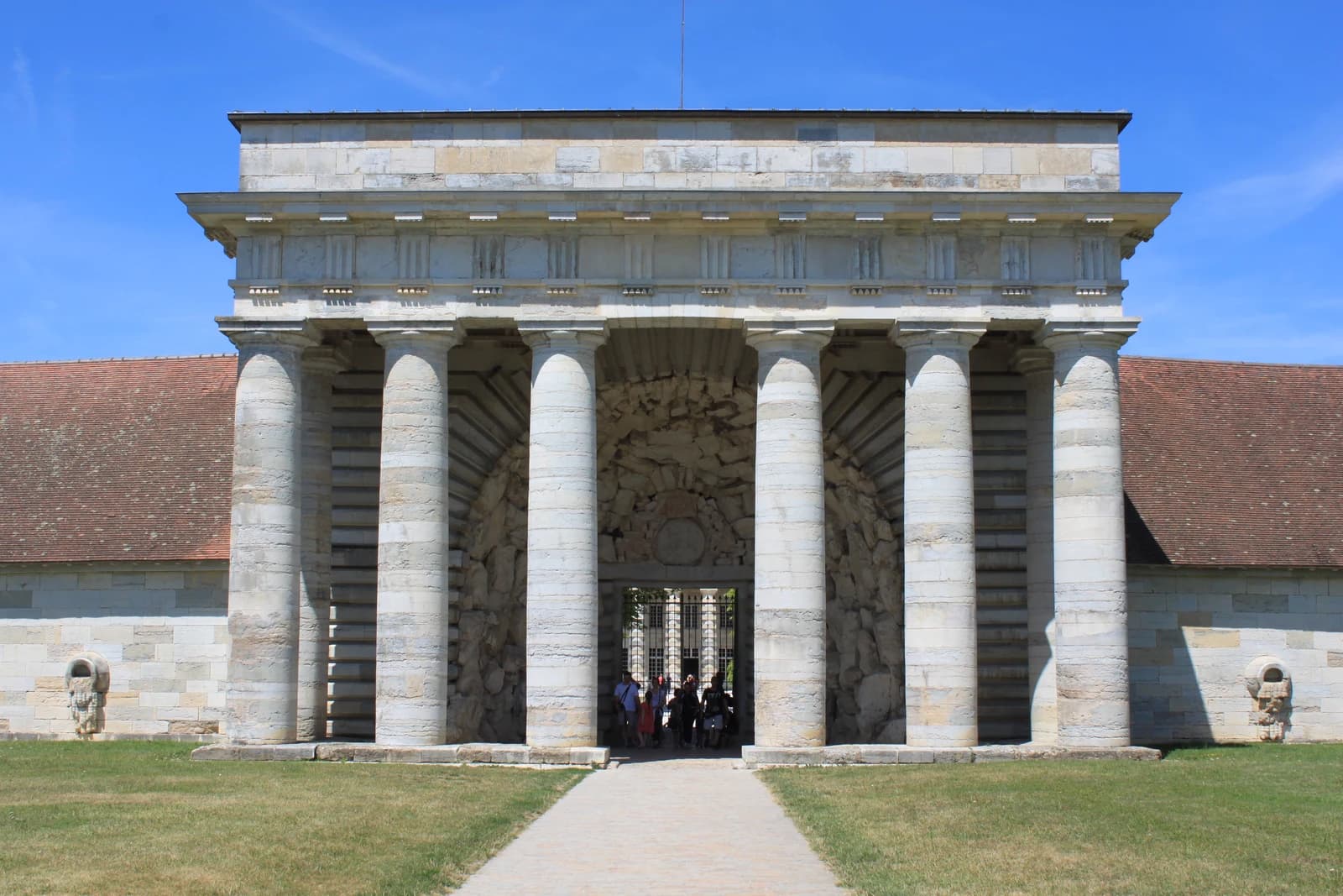 The monumental columned entrance of the Royal Saltworks at Arc-et-Senans beneath a blue sky.