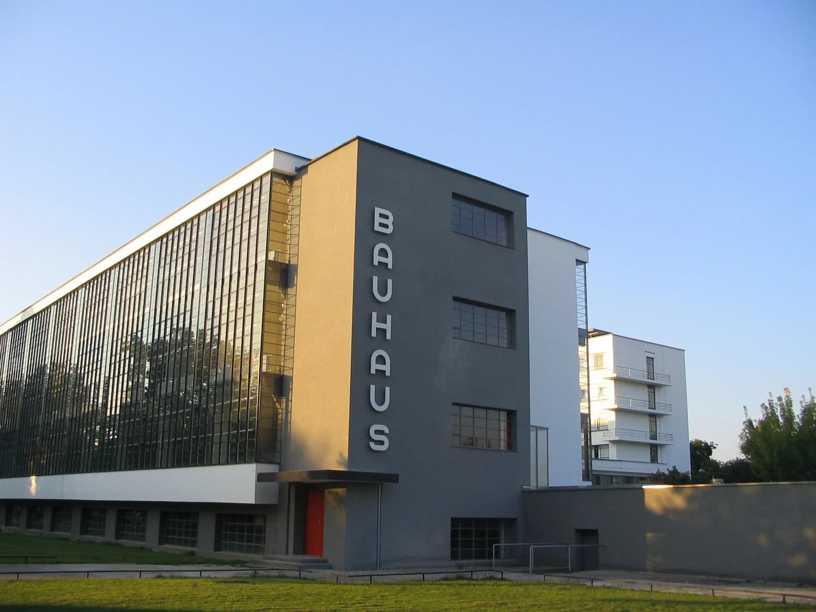 The glass workshop wing and white walls of the Bauhaus Building in Dessau under a blue sky.
