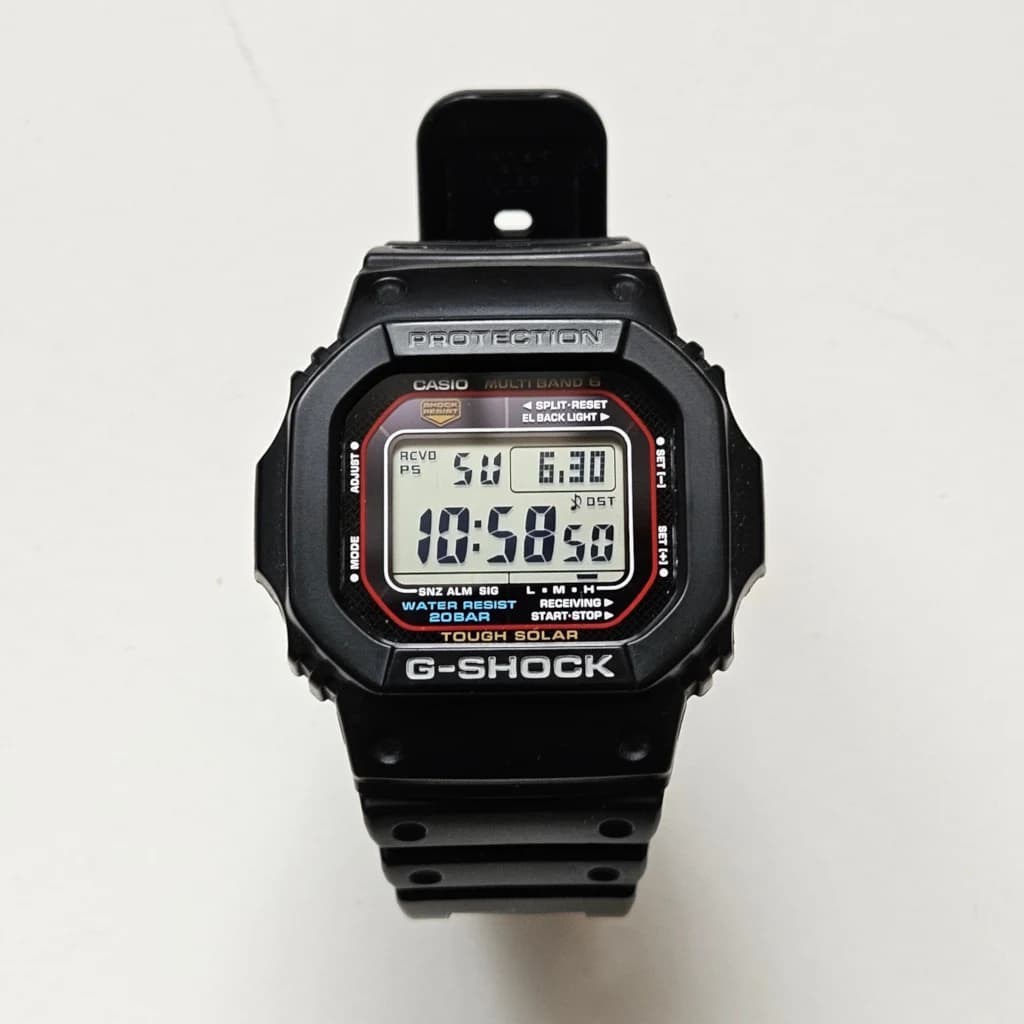 A black Casio G-SHOCK GW-M5610 digital watch with a red-bordered display on a white background.