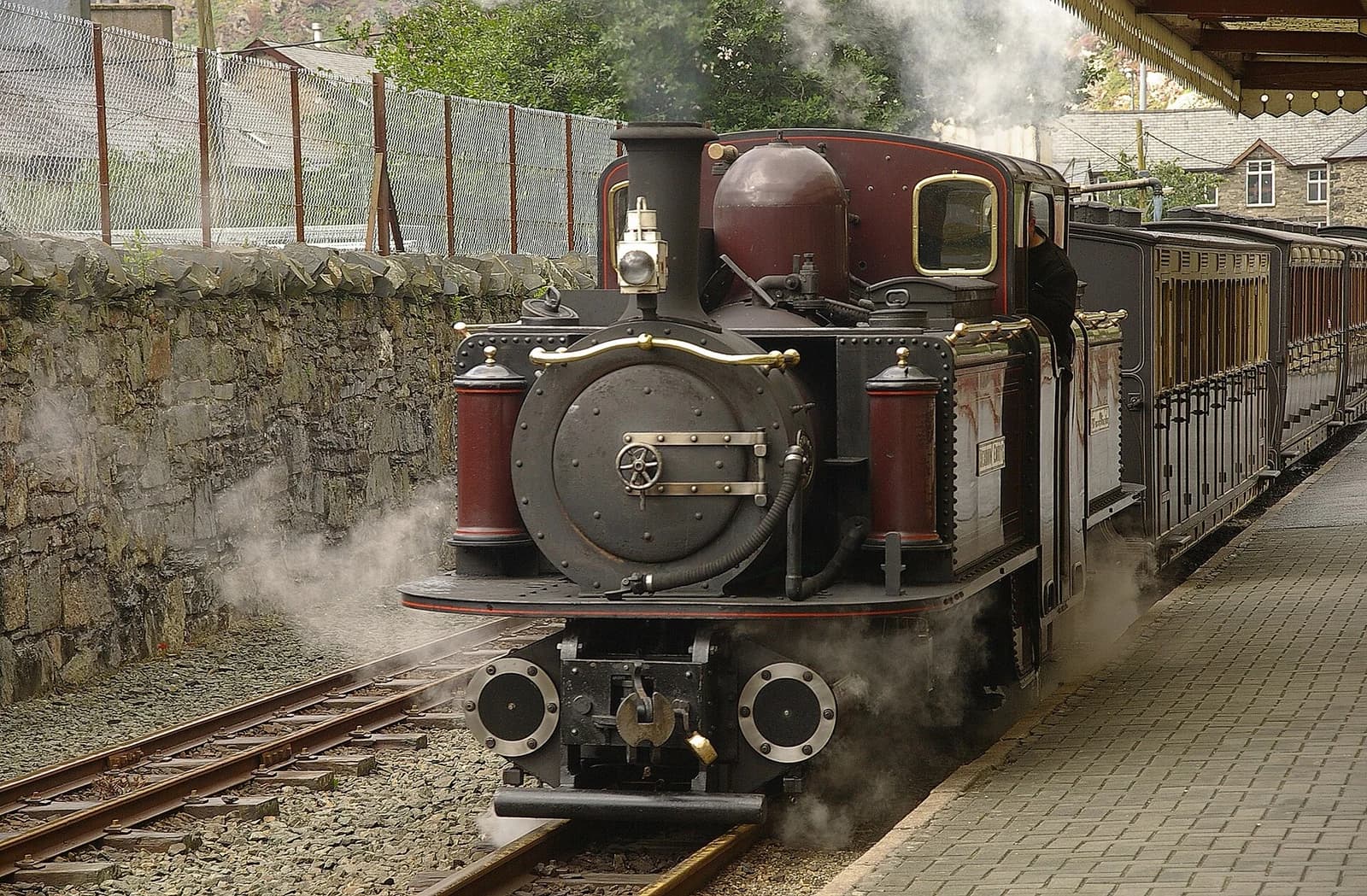 The red double Fairlie locomotive Merddin Emrys arrives at Blaenau Ffestiniog with steam rising above it.