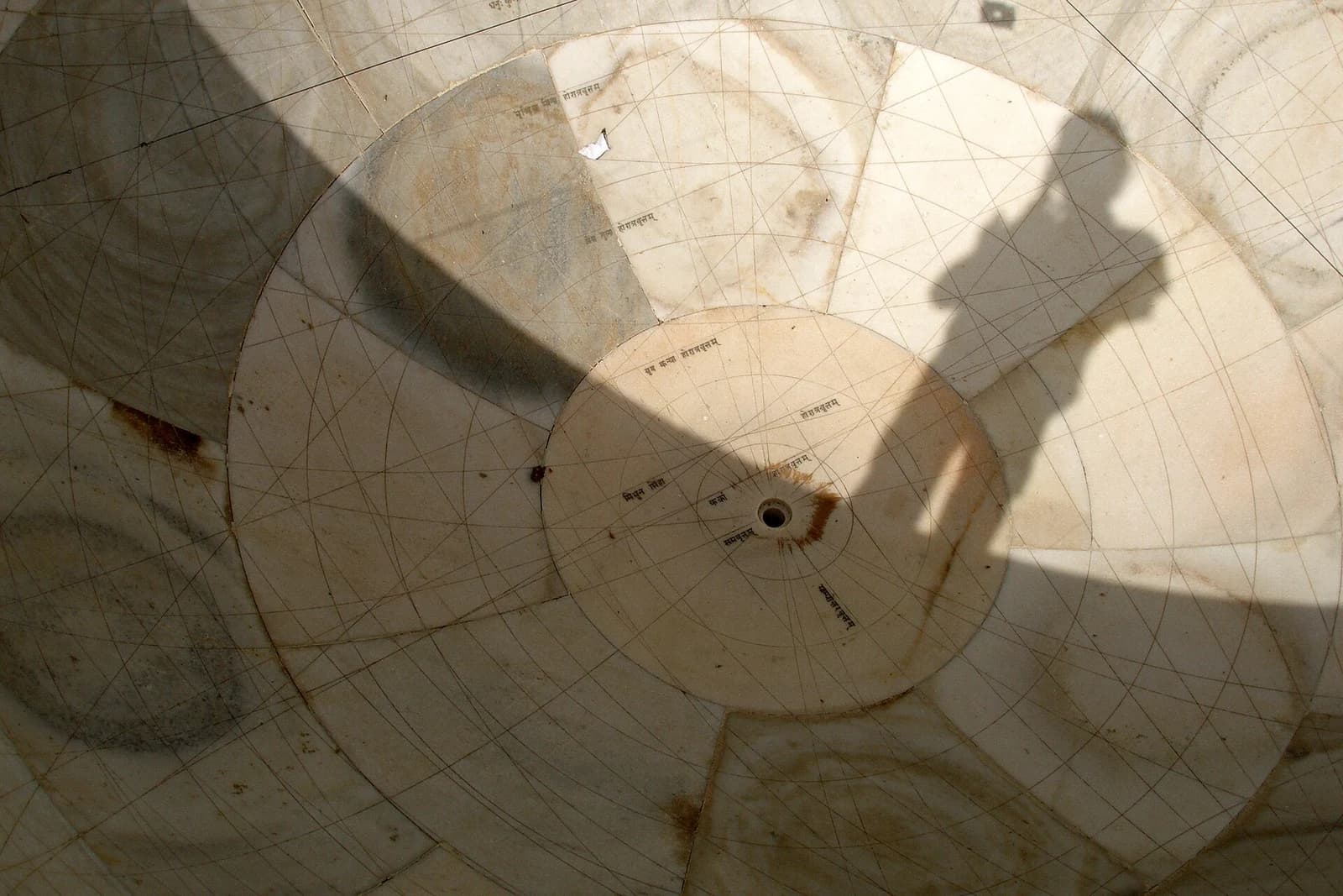 Curved marble scales descend into a hemispherical astronomical instrument at Jantar Mantar, with a shadow above.