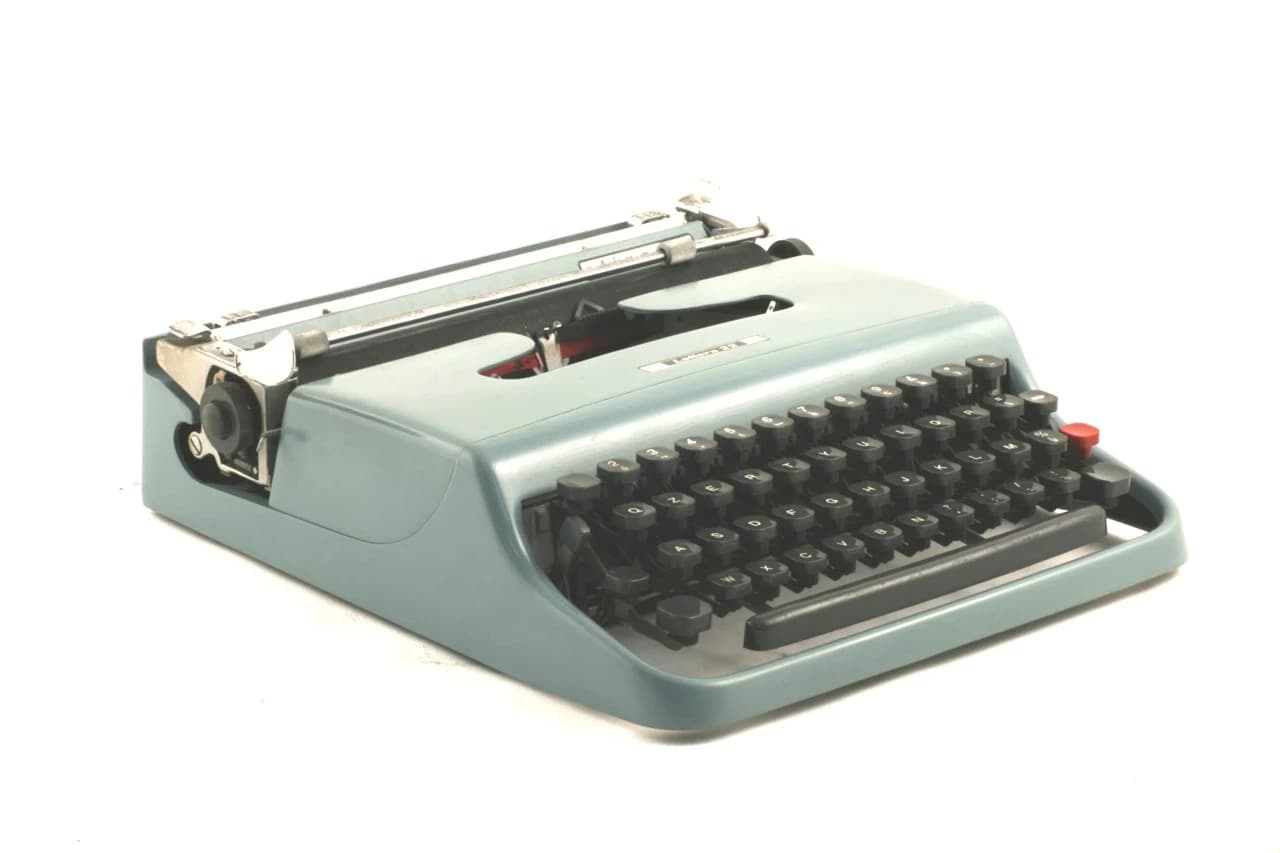 A pale blue Olivetti Lettera 22 portable typewriter with grey keys, photographed against white.