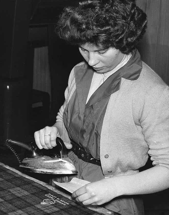 A woman applies the Orb certification mark to Harris Tweed cloth in a black-and-white photograph.
