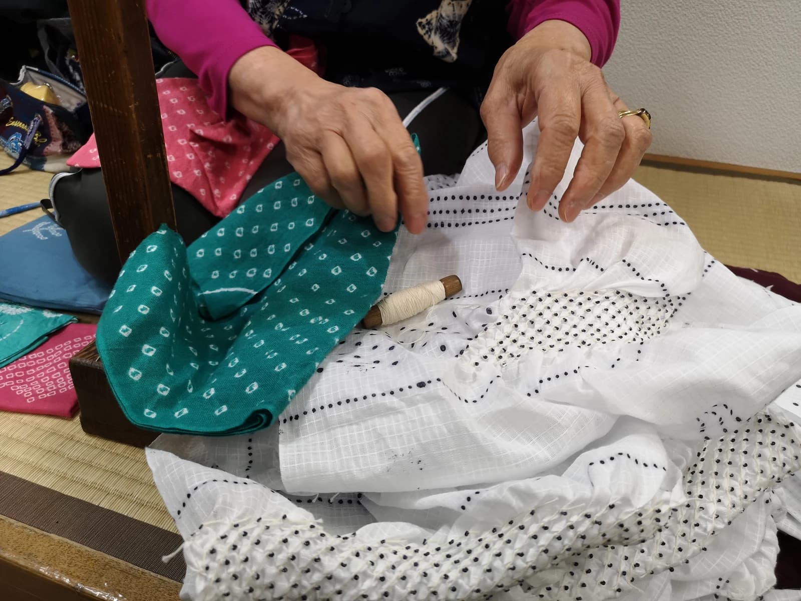 Hands demonstrate bound white shibori cloth beside a green dyed sample with pale repeated circular marks.