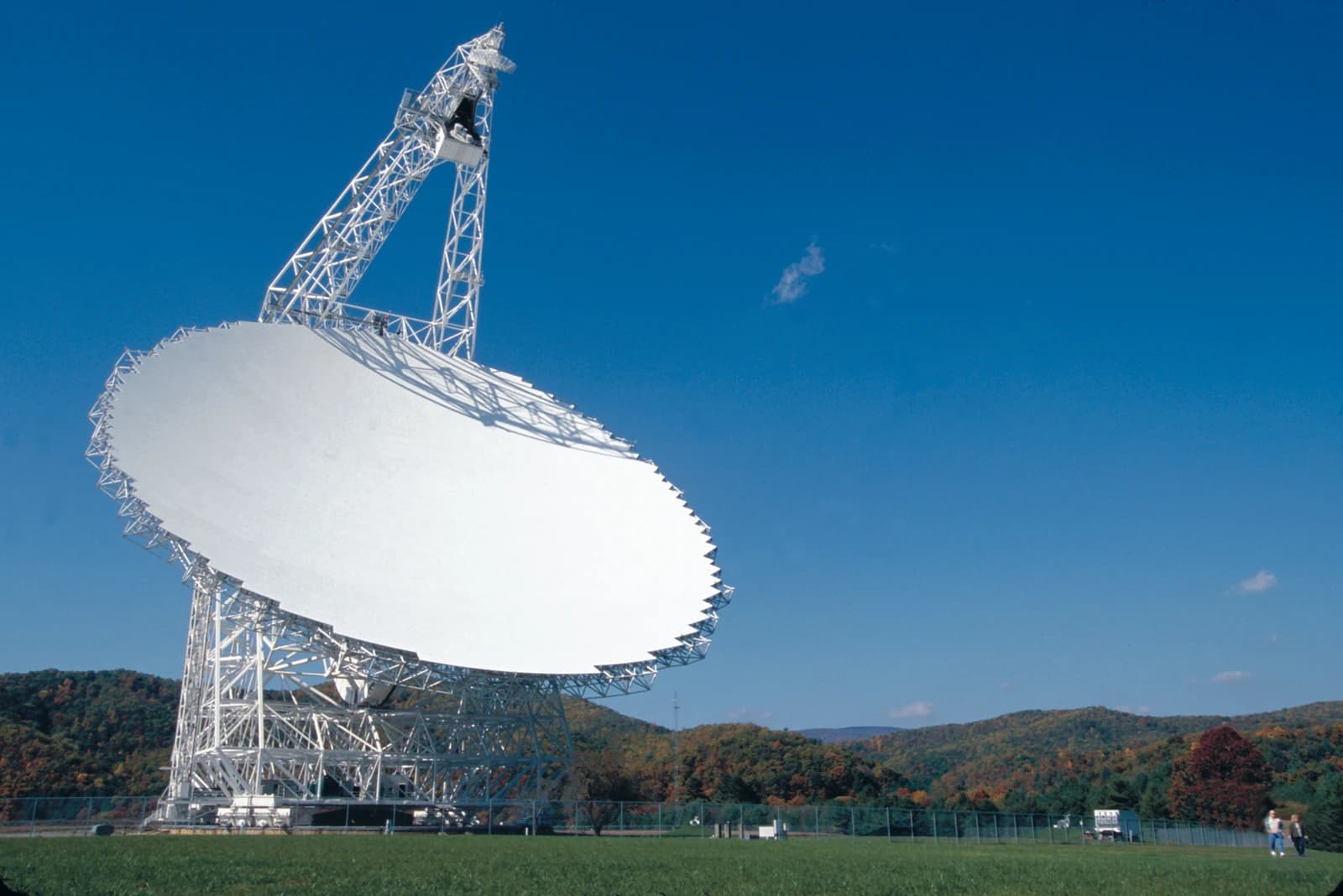 The white dish and steel framework of the Green Bank Telescope rise above trees against a deep blue sky.