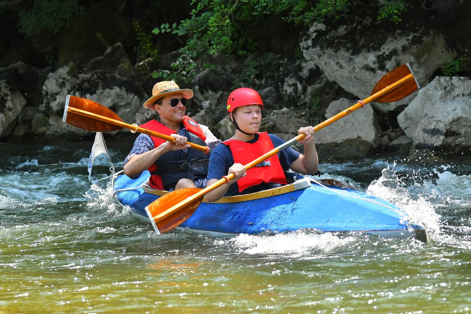 Two paddlers in buoyancy aids navigate an Ardèche river section in a blue Klepper Aerius II folding kayak.