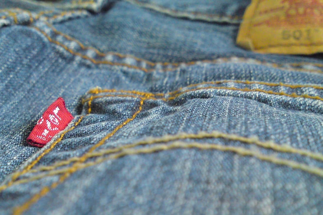 Close view of worn blue denim, yellow pocket stitching and the red Levi’s tab on a pair of 501 jeans.