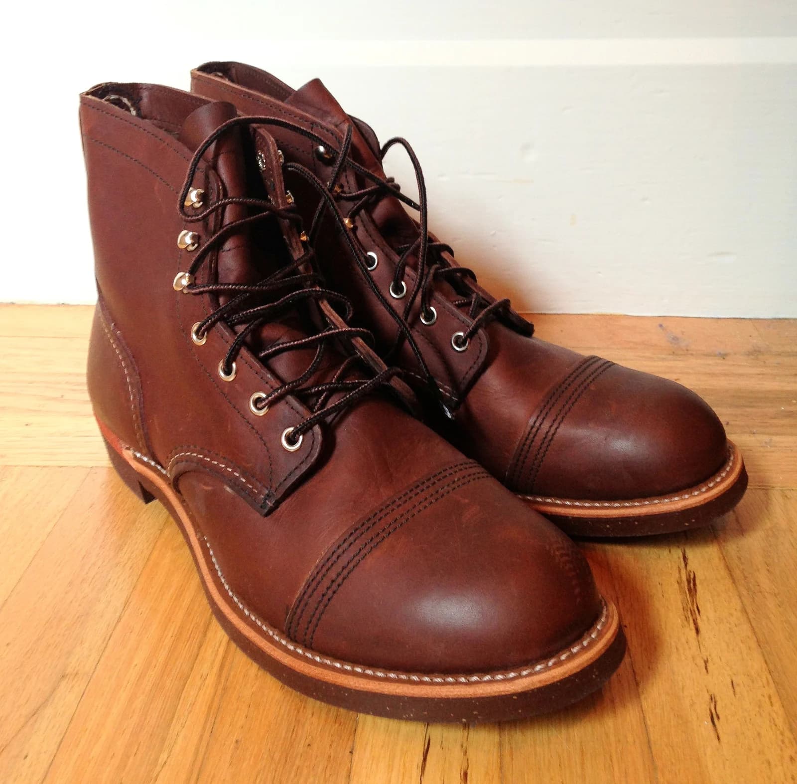 A pair of brown Red Wing Iron Ranger boots showing cap toes, stitching, leather welts and laces on a wooden surface.