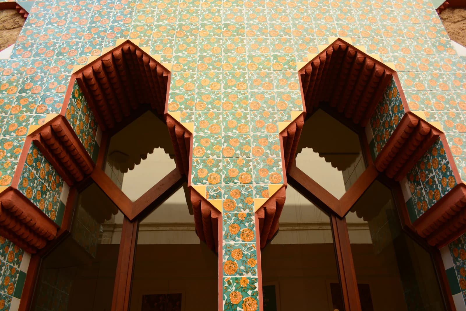 Turquoise tiles with yellow floral motifs surround deeply shaped red-brown window openings at Casa Vicens.