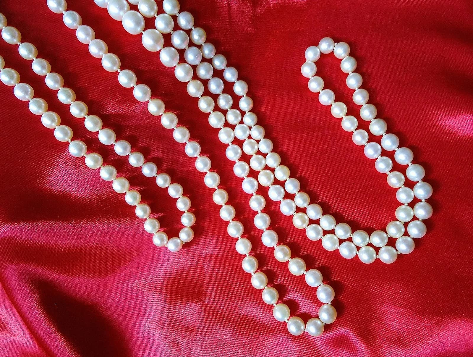 Several strands of pale cultured pearls sweep across deep red satin under strong light.