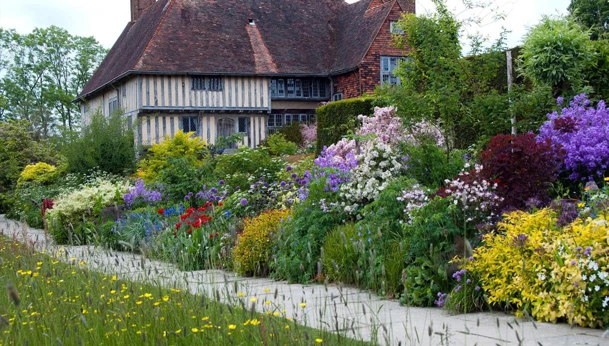 Great Dixter’s long border in full colour beside a stone path, with the timbered house rising behind layered planting.