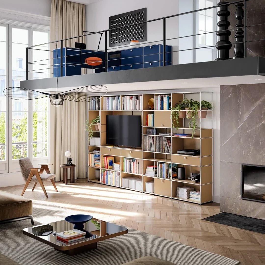 A pale USM Haller modular wall holds books, plants and a television in a sunlit living room, with blue cabinets on the mezzanine above.