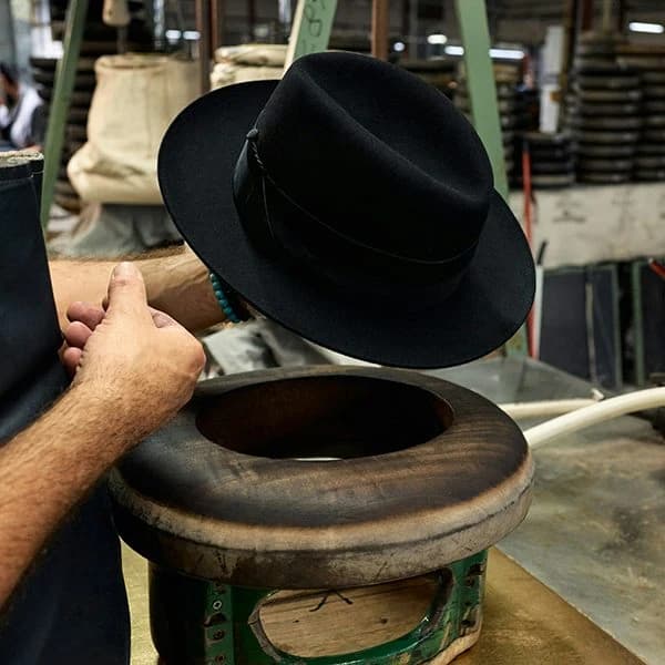 A workshop worker holds a dark felt hat beside hat-making equipment in Borsalino’s published hat-care imagery.