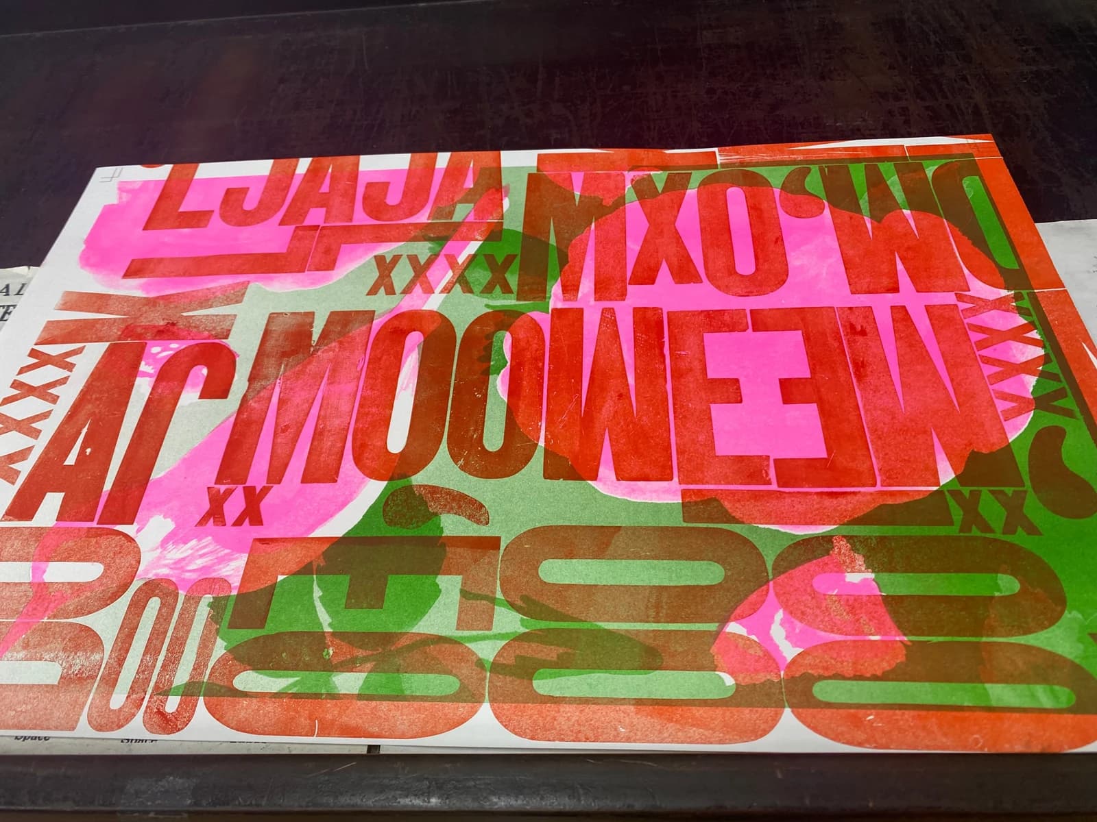 Overlapping red, pink and green letterpress forms fill a sheet with abstract typographic shapes and fragments of letters.