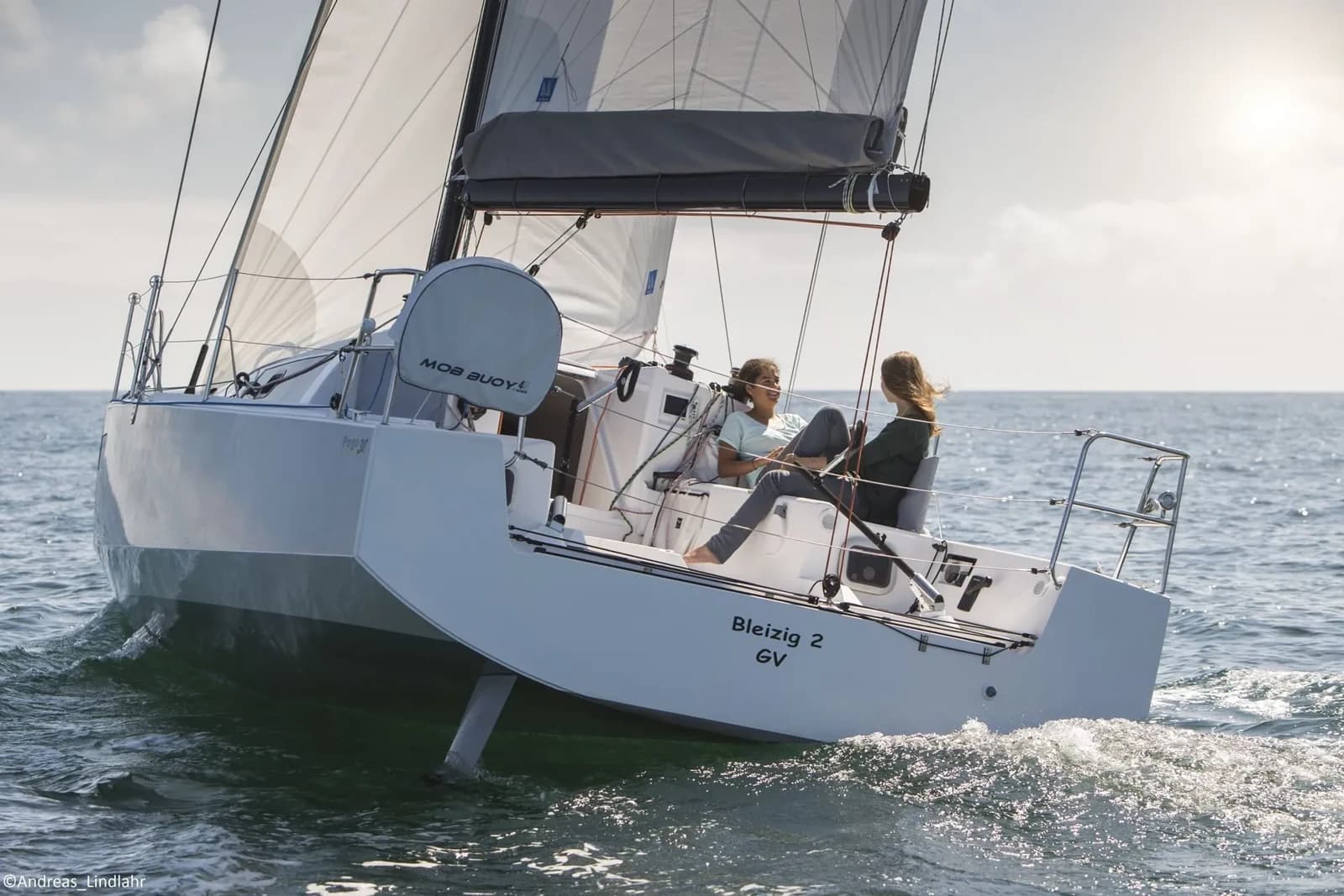 The Pogo 30 Bleizig 2 sails under white sails on blue water, photographed from a low angle beside the hull.