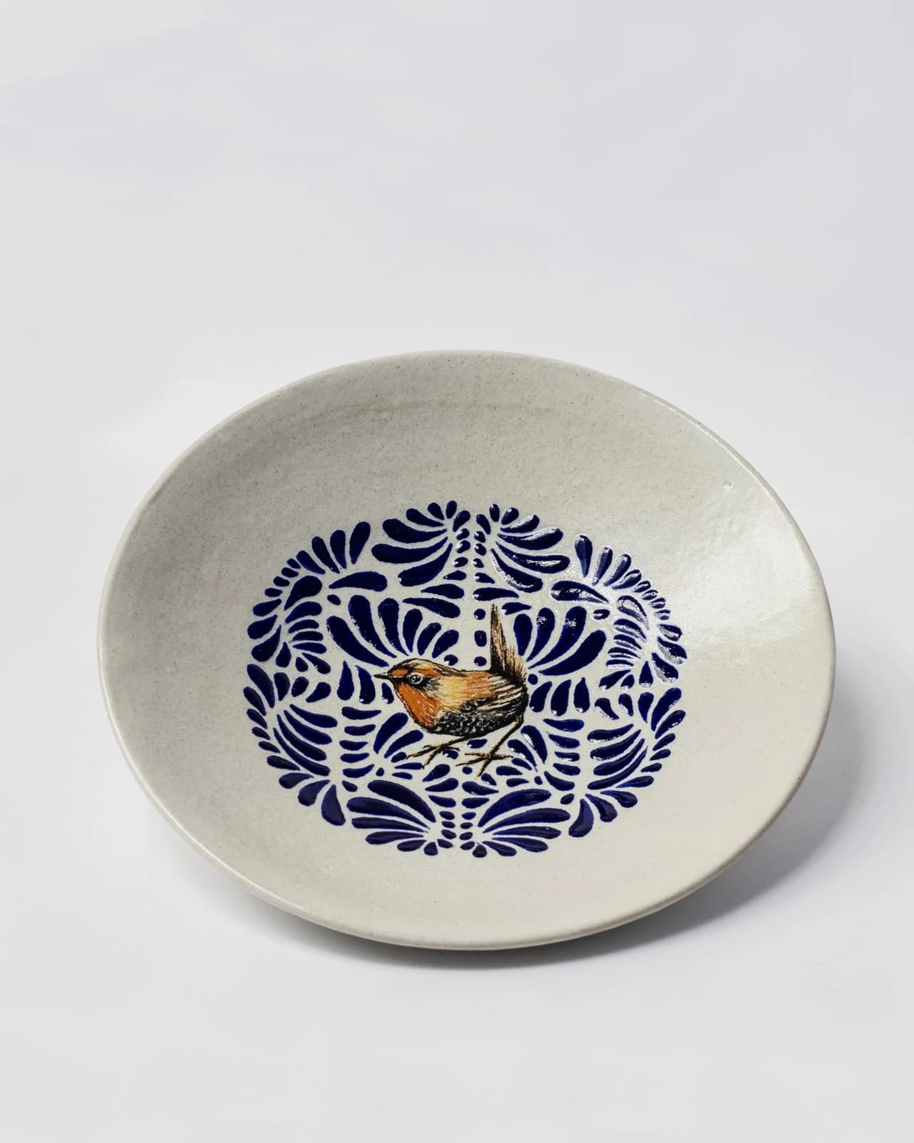 A Uriarte Aves decorative Talavera plate with a central bird and blue painted foliage, photographed against a light background.