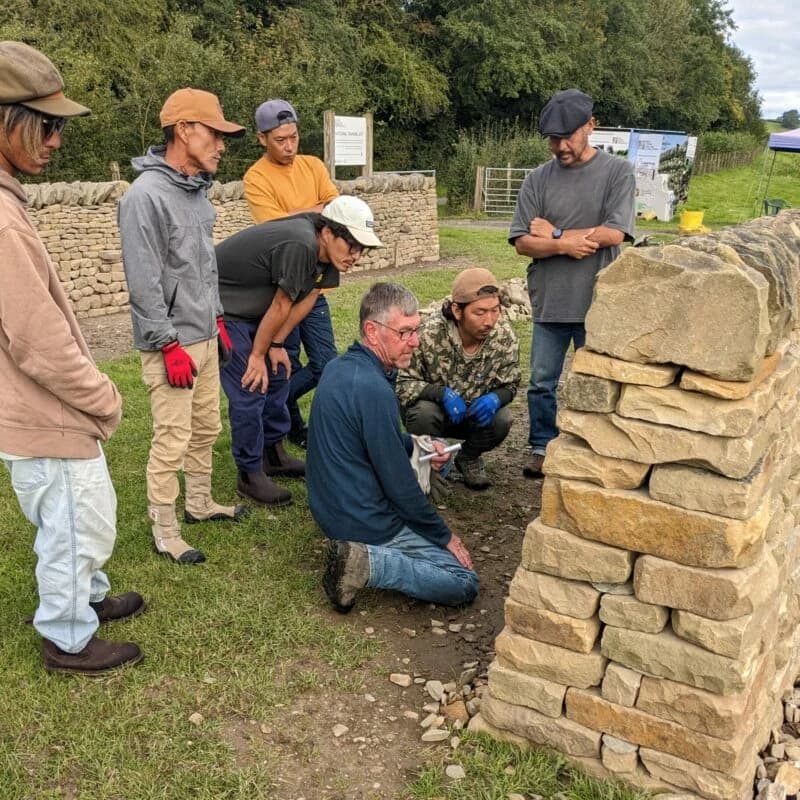 A group of learners examines a dry-stone wall outdoors at the Dry Stone Walling Association’s training site.