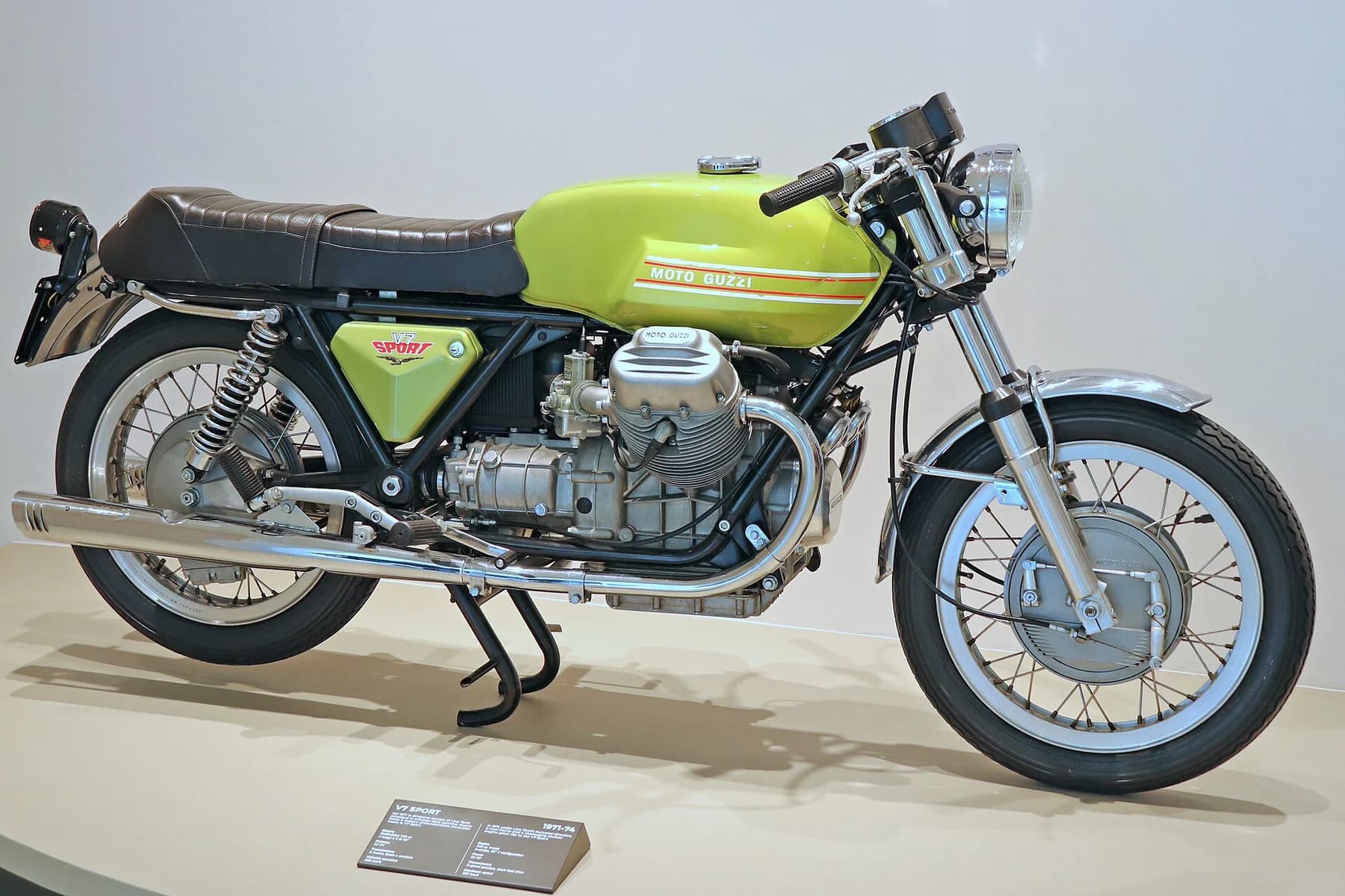 A historic lime-green Moto Guzzi V7 Sport motorcycle in side profile at the Moto Guzzi Museum, with its exposed engine and wire wheels.