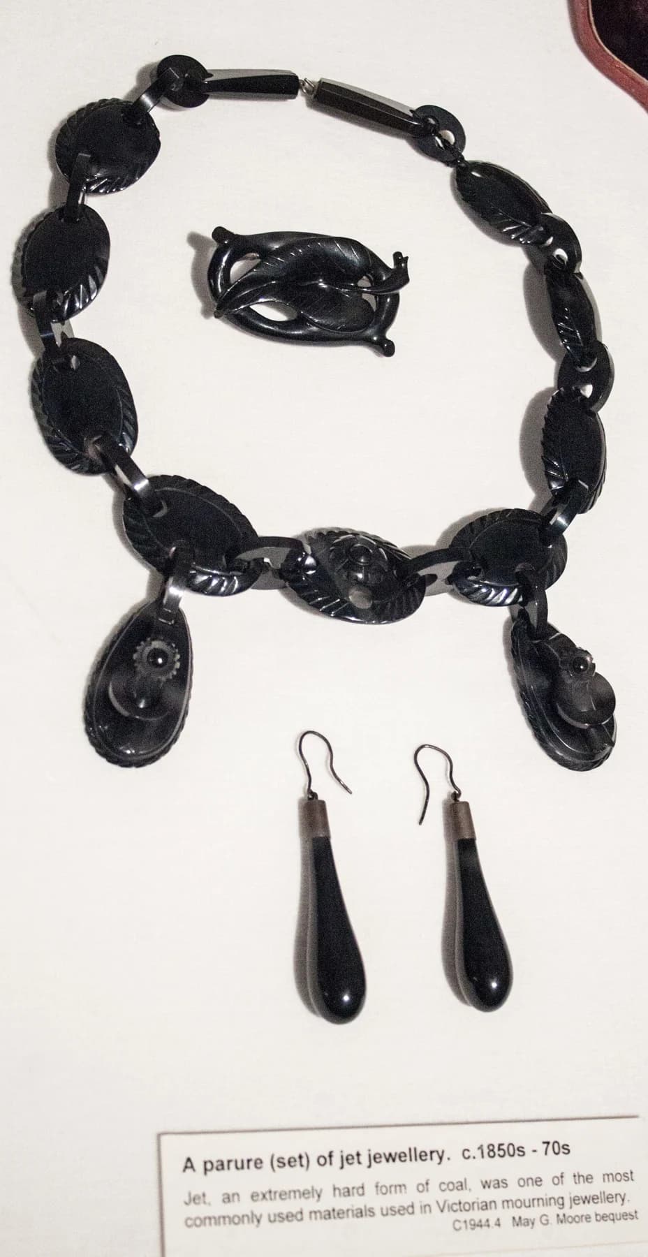 A black jet necklace, brooch and two drop earrings displayed on a pale panel at Canterbury Museum, with the museum label below.