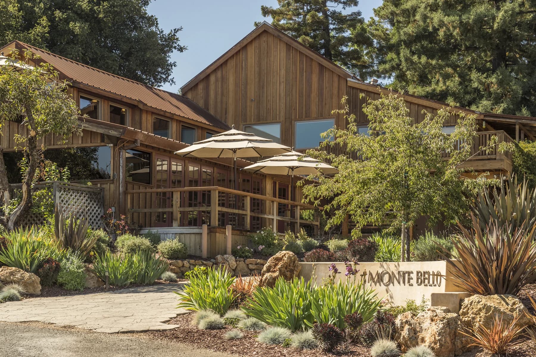 Ridge’s timber Monte Bello winery buildings sit among trees and planted terraces, with a Monte Bello sign beside the path.