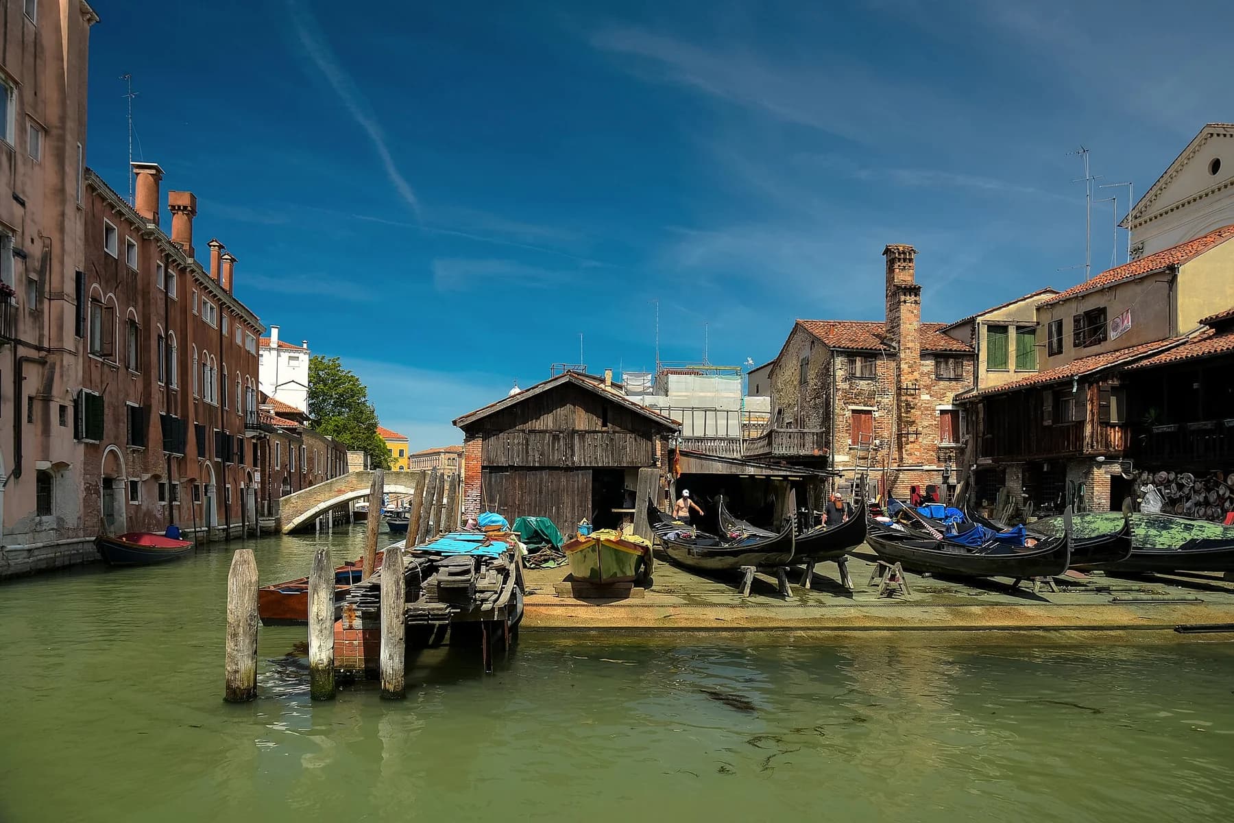 Gondolas and working boats rest in the sloping yard of Squero di San Trovaso, with its timber shelter and a Venice canal beside it.