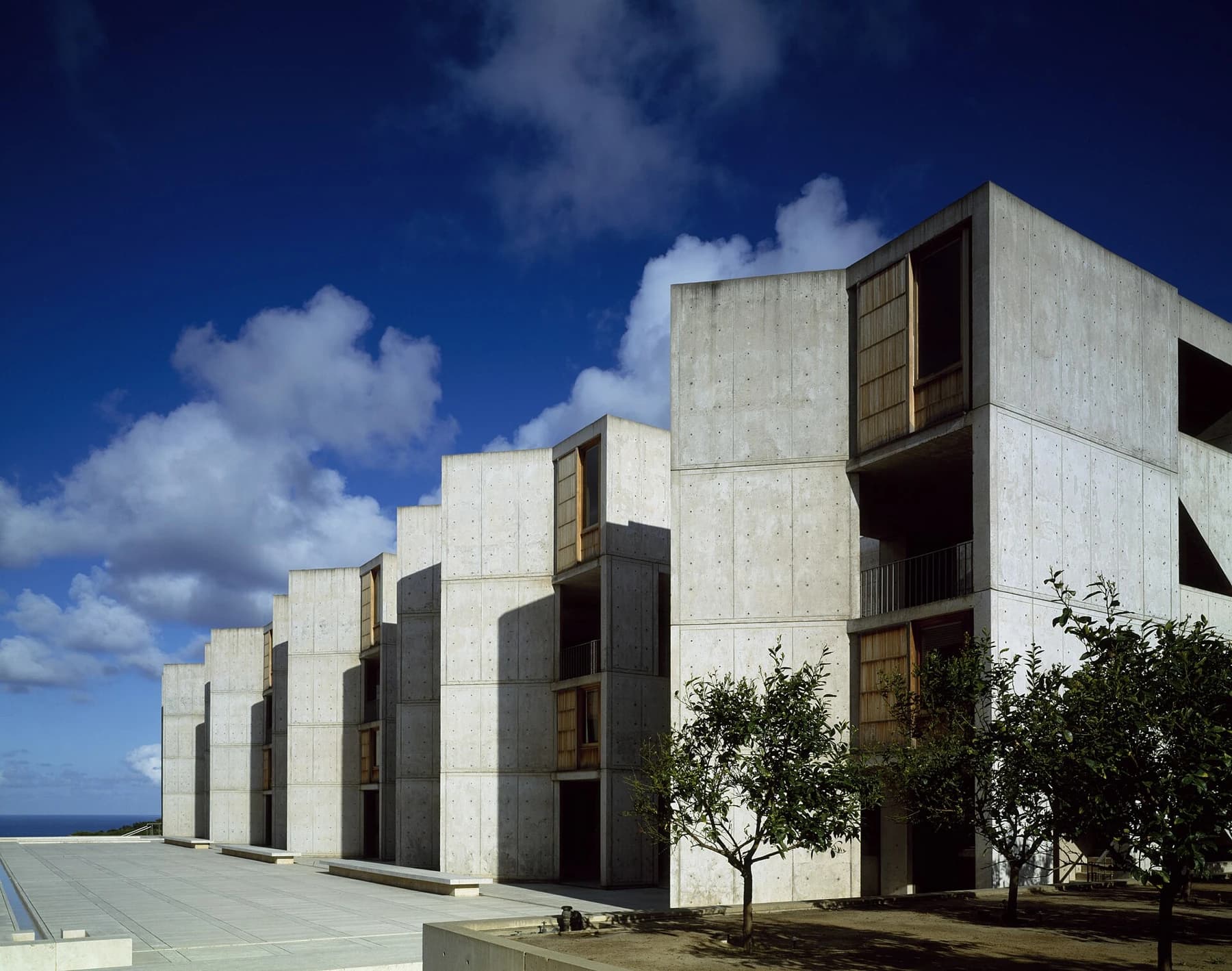Louis Kahn’s concrete laboratory buildings and timber study windows at the Salk Institute stand against a deep blue California sky.