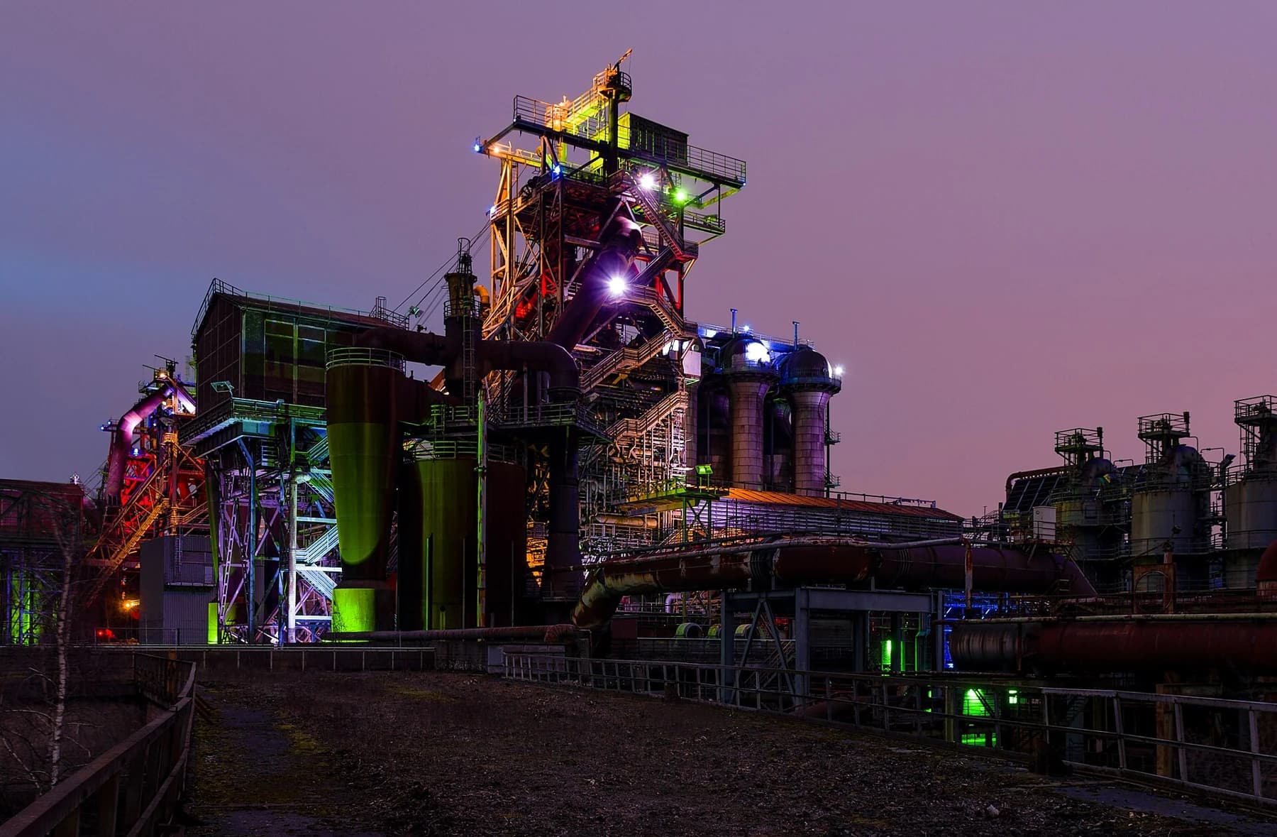 Blast Furnace 5 at Landschaftspark Duisburg-Nord illuminated in green, yellow and violet beneath a purple evening sky.