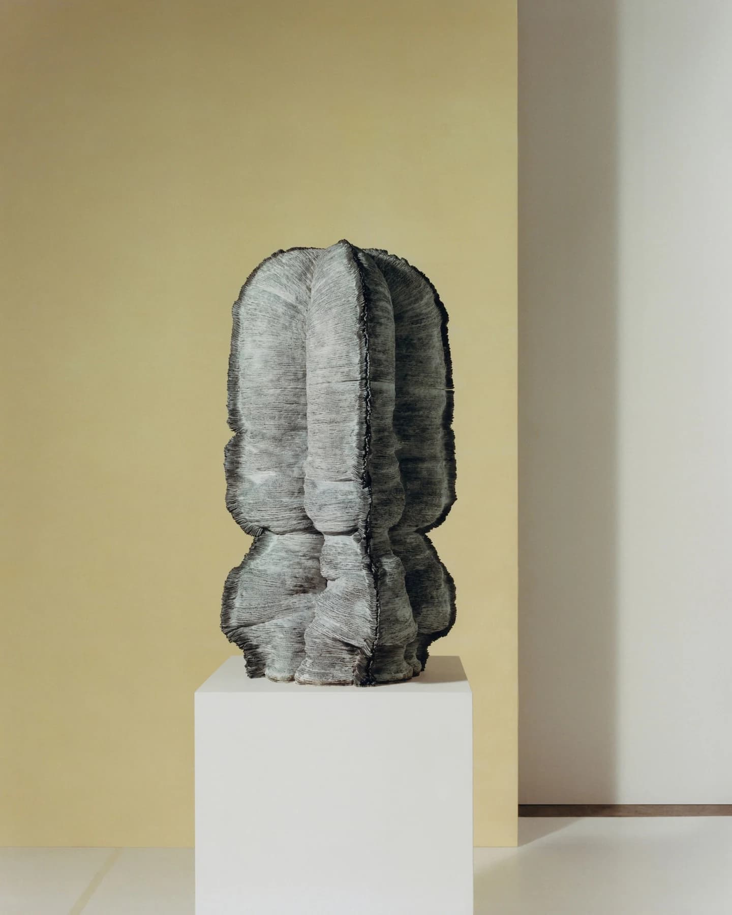 Kunimasa Aoki’s Realm of Living Things 19, a grey terracotta sculpture with compressed layers and an irregular upright form, displayed on a pale plinth.