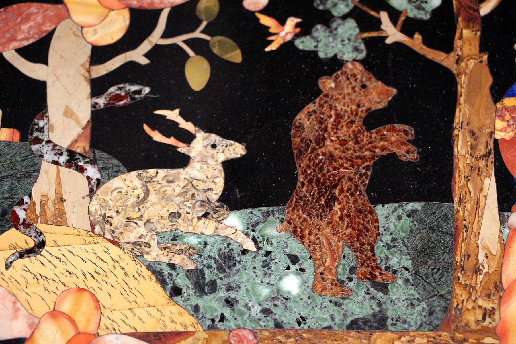 A historical Florentine hardstone-inlay detail depicting animals and plants, with patterned coloured stones fitted into a dark ground.