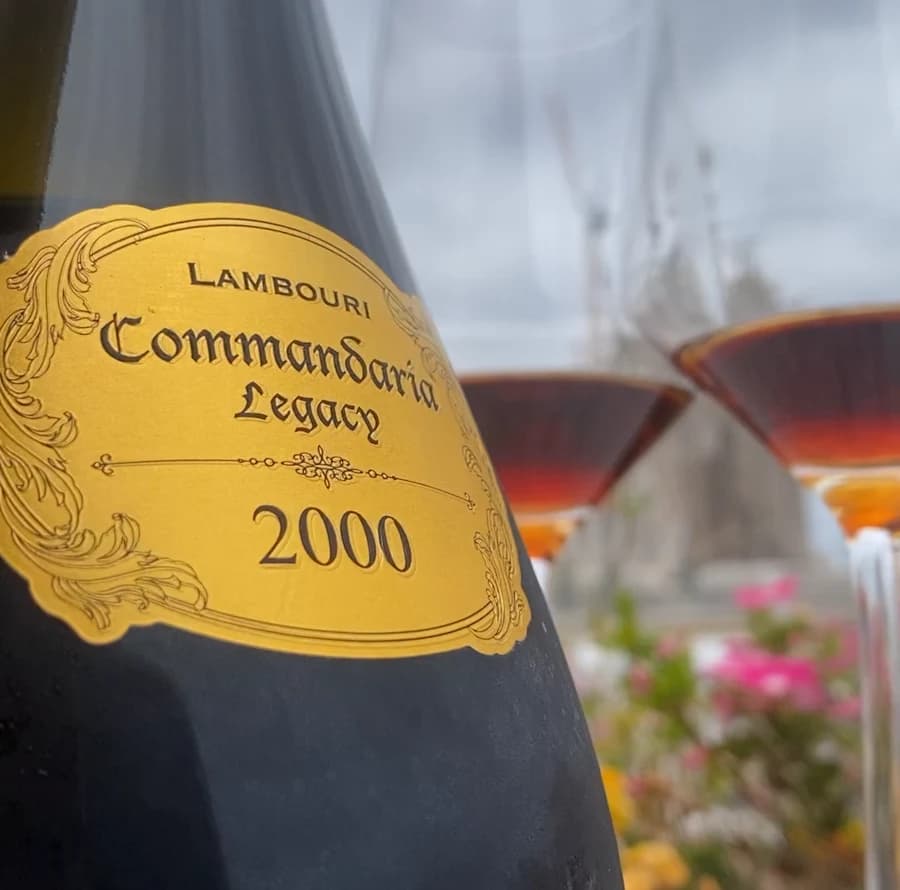A bottle labelled Lambouri Commandaria Legacy 2000 beside glasses of amber wine, with the gold label in the foreground.