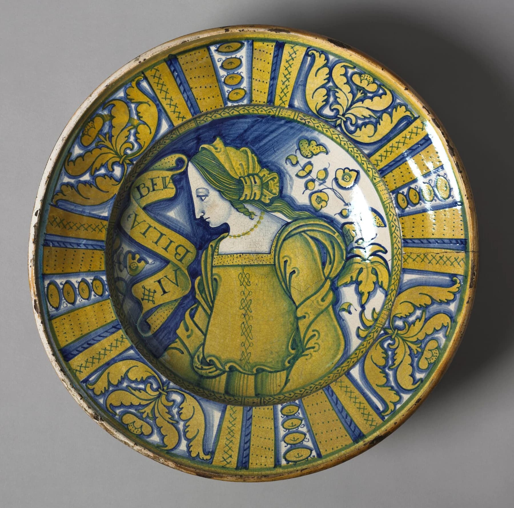 A Deruta maiolica charger with a woman’s profile at its centre and a wide rim decorated in yellow and blue lustre.