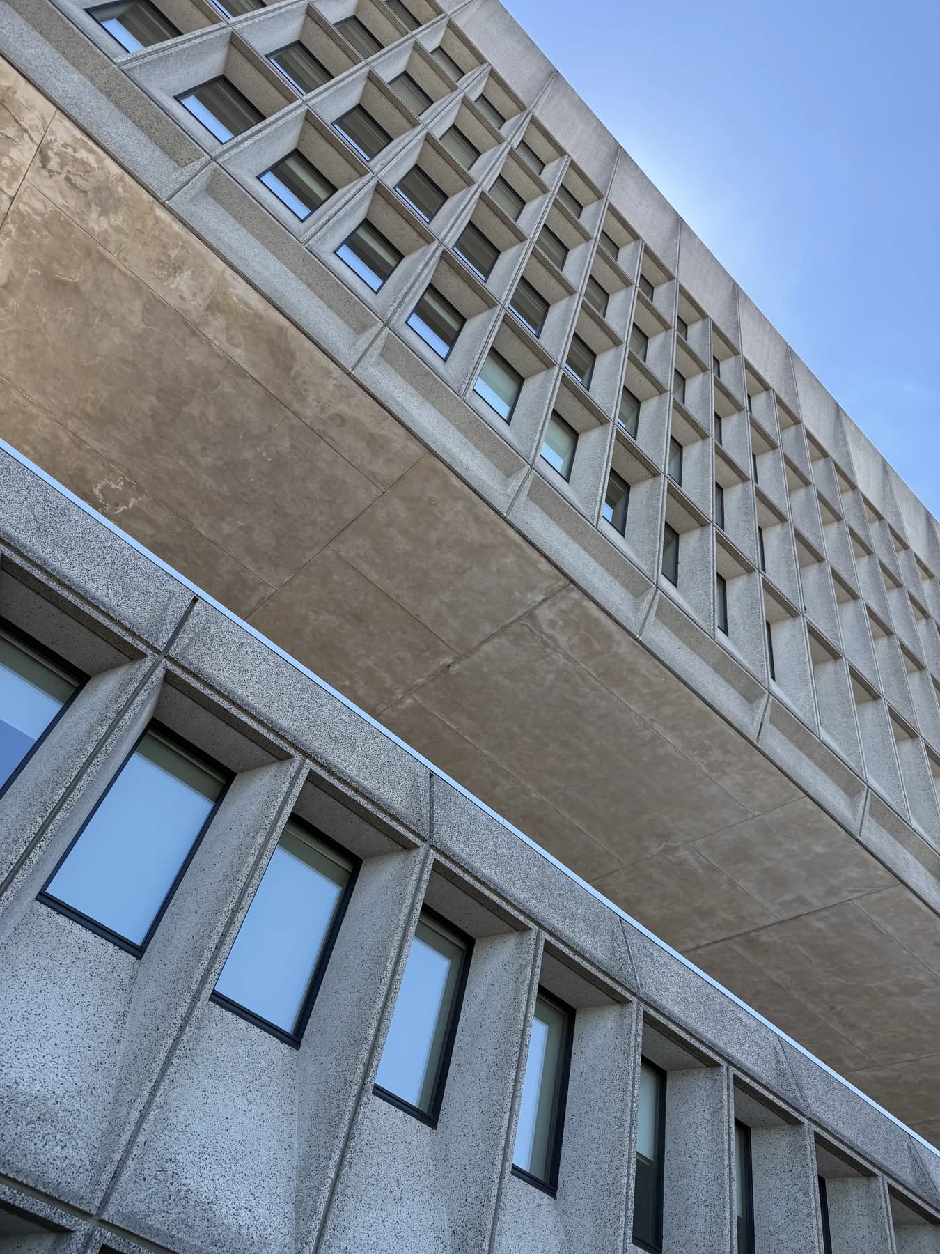 An upward view of Hotel Marcel’s concrete facade in New Haven, showing repeated window bays and the open gap between the building’s masses.