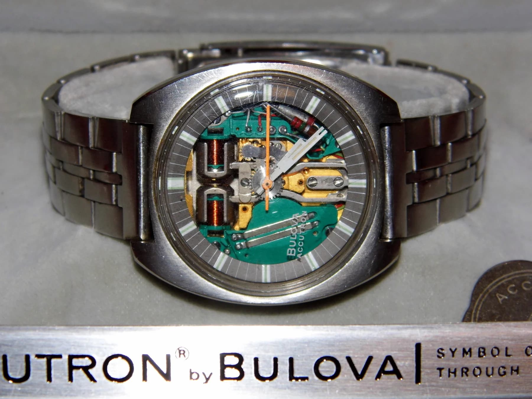 A vintage Bulova Accutron Spaceview in its display box, with green electronic components, copper coils and the tuning-fork mechanism visible beneath the hands.