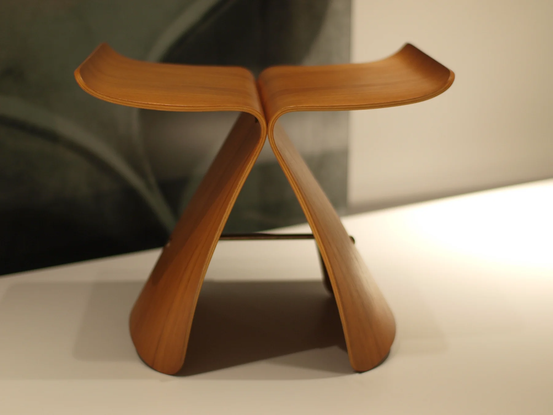 A warm-toned Butterfly Stool seen from the front, its two curved plywood halves rising from the floor into an upswept seat.