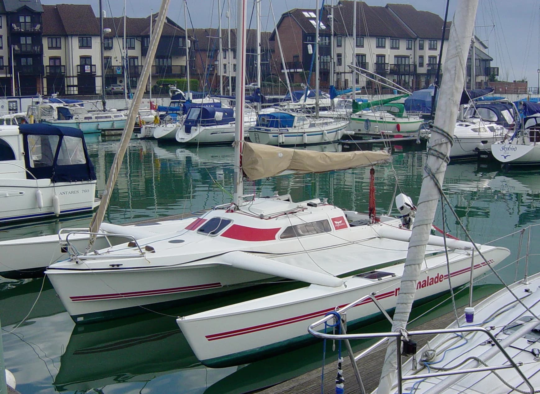 An earlier white and red Dragonfly trimaran sits in a marina with its outer hulls extended and connected to the central hull by broad arms.