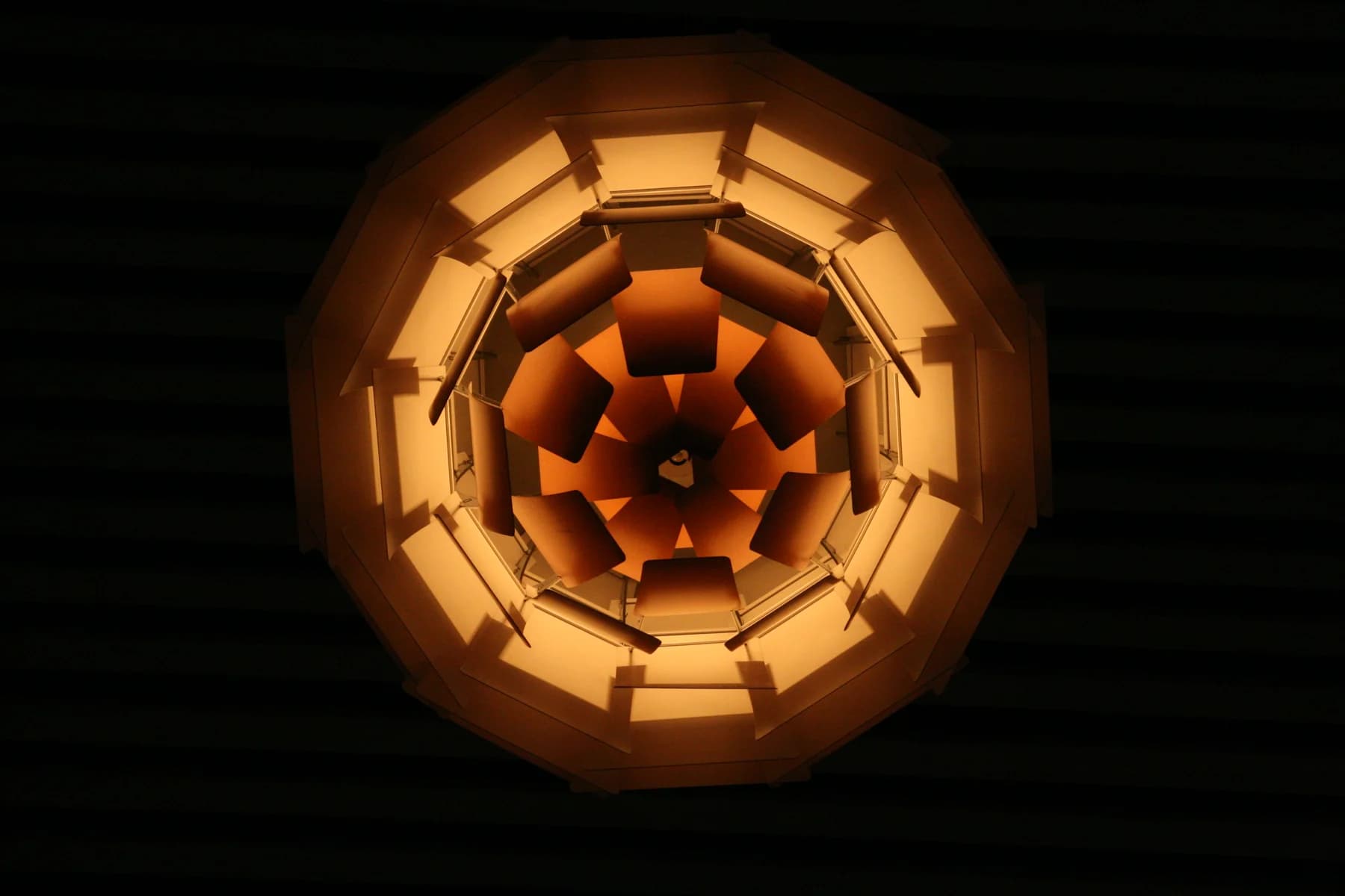 An illuminated copper PH Artichoke lamp seen directly from below, its layered leaves glowing gold against a dark ceiling.
