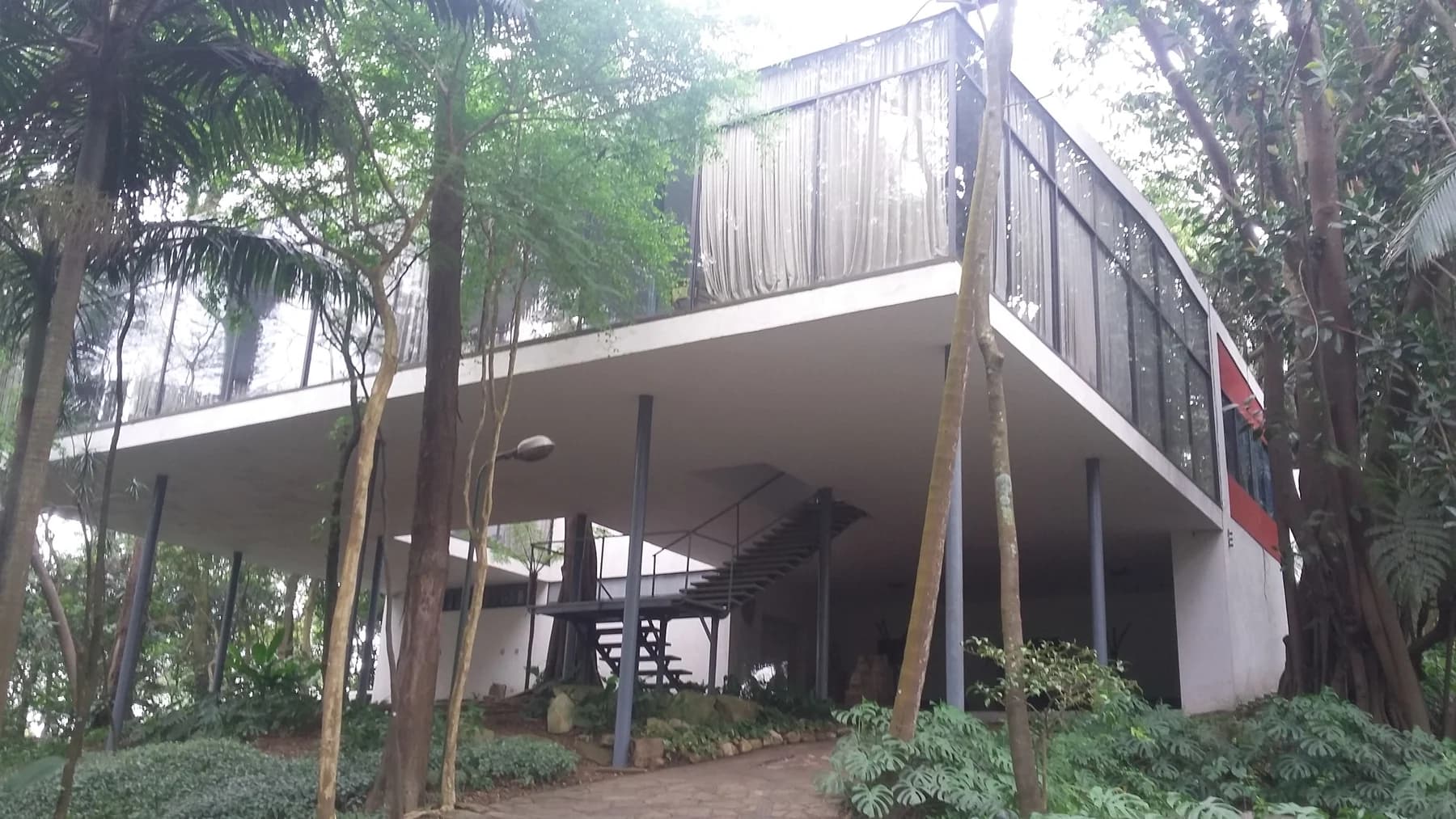 Lina Bo Bardi’s Casa de Vidro raised on slender supports among trees, with glass walls above an open ground-level approach.