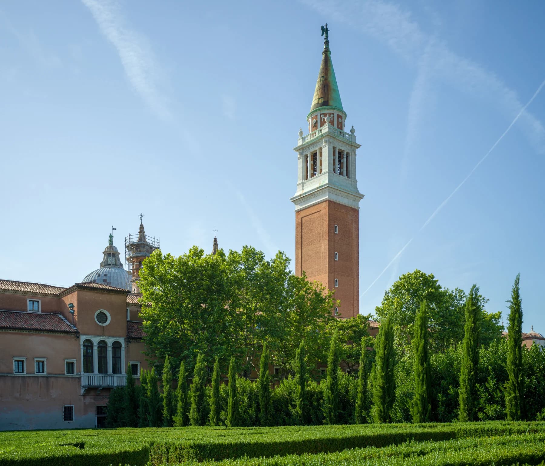 The campanile of San Giorgio Maggiore rising above trees, with low labyrinth hedges across the foreground under a blue Venetian sky.