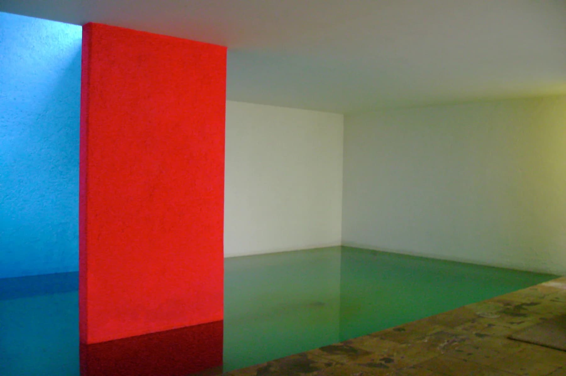 A vivid red vertical plane beside a blue wall and pale green indoor pool at Casa Gilardi in Mexico City.