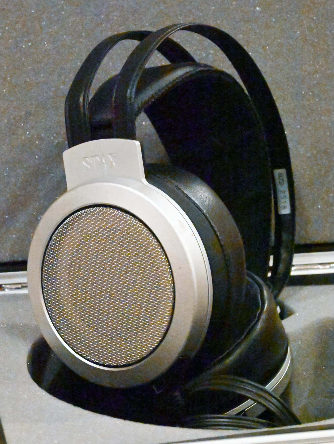 Silver-and-black STAX SR-007A electrostatic headphones resting on a stand, with their circular mesh enclosure and padded headband visible.