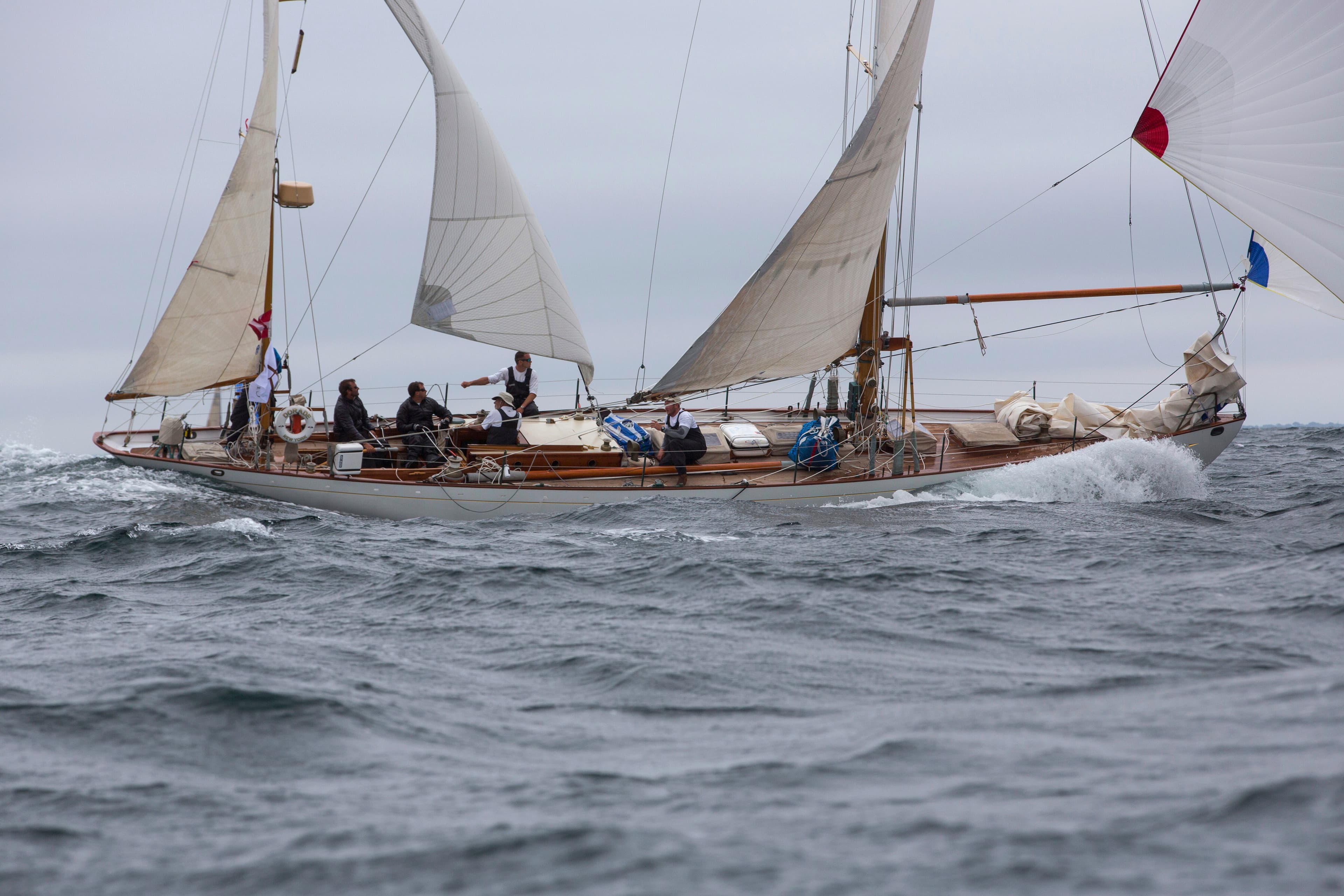 The restored wooden yawl Dorade sailing hard in grey water with her crew working on deck.