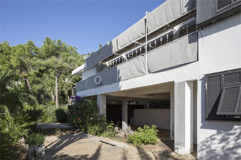 The restored white exterior of Eileen Gray’s E-1027 with grey canvas screens and Mediterranean planting.