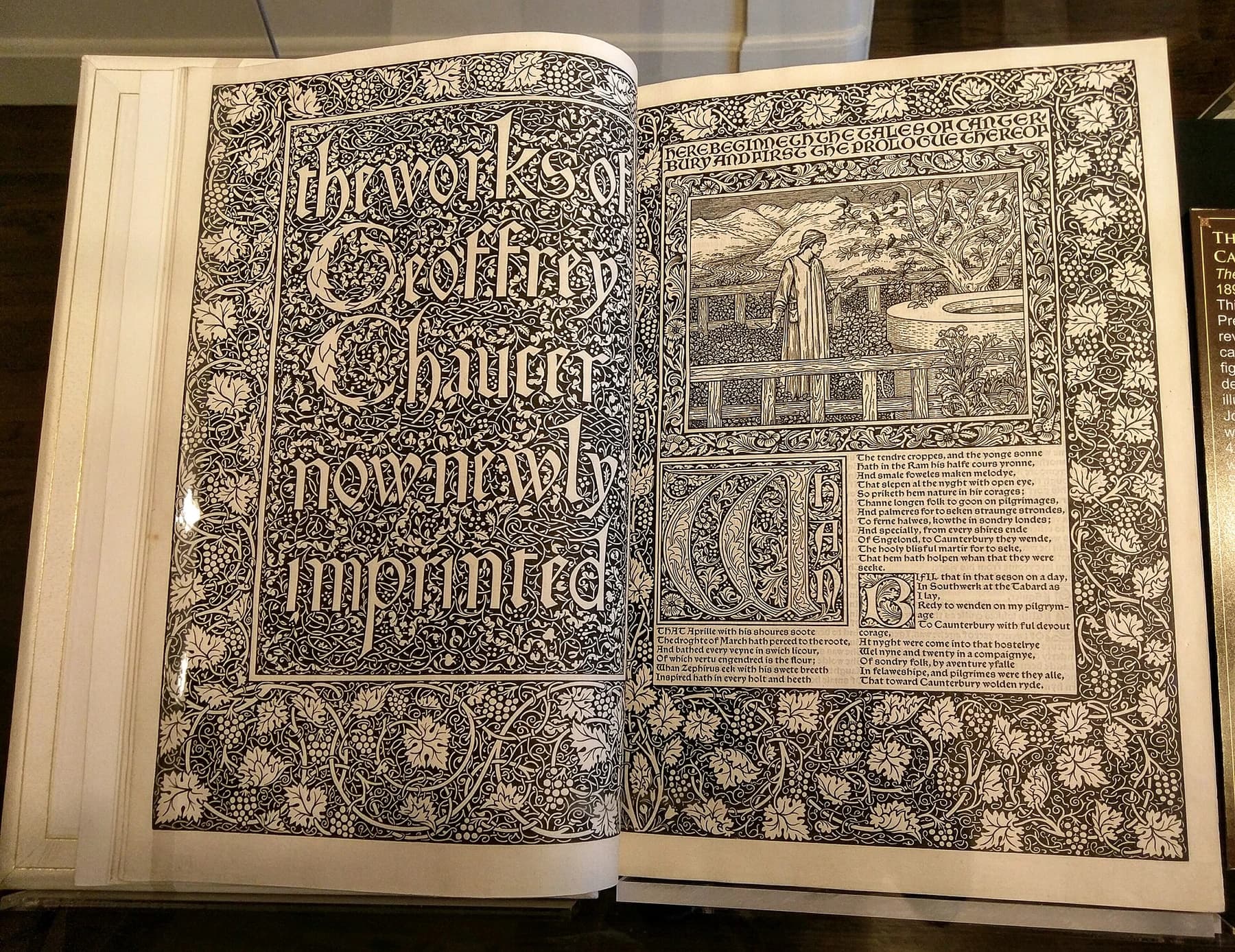An open Kelmscott Chaucer showing two densely ornamented pages of black type, decorated initials and floral borders on cream paper.