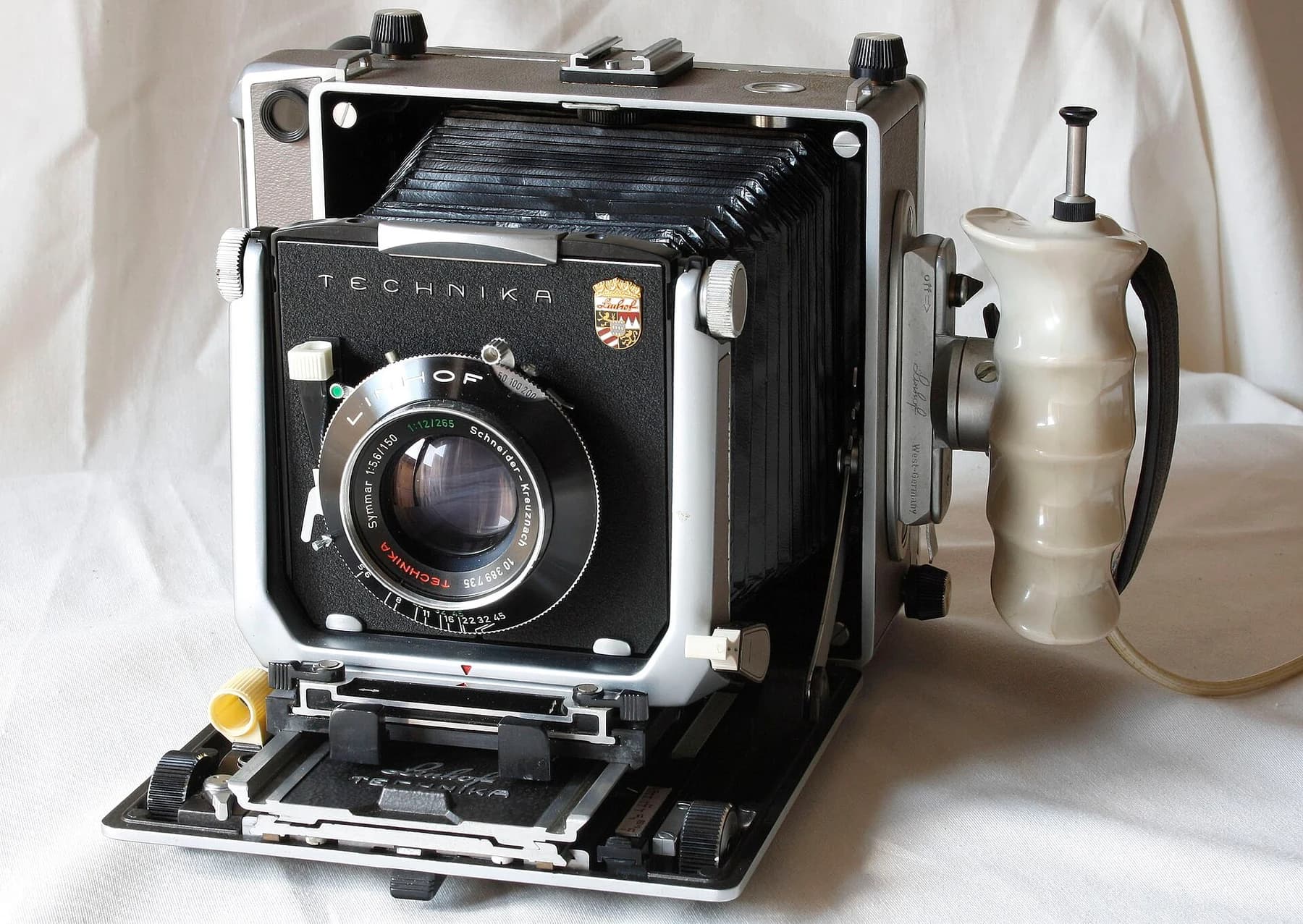 A Linhof Super Technika V camera with its black bellows extended and lens mounted on the front standard, isolated against a pale background.