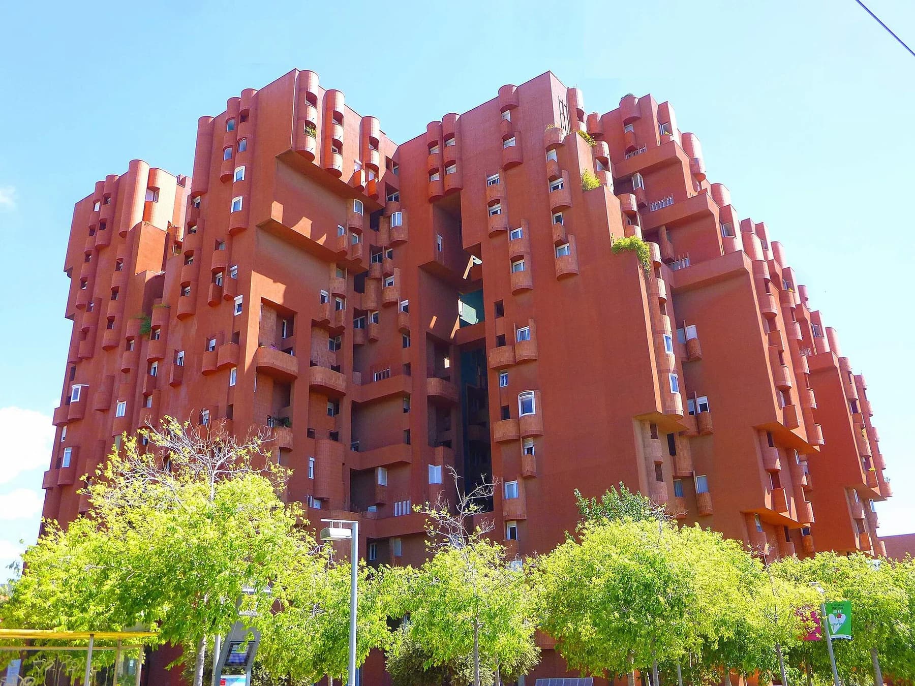 Walden 7’s connected red apartment towers rising above green trees under a clear blue sky in Sant Just Desvern.
